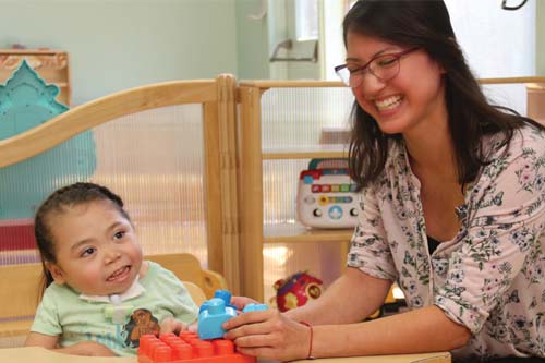 Staff playing blocks on a table with a girl